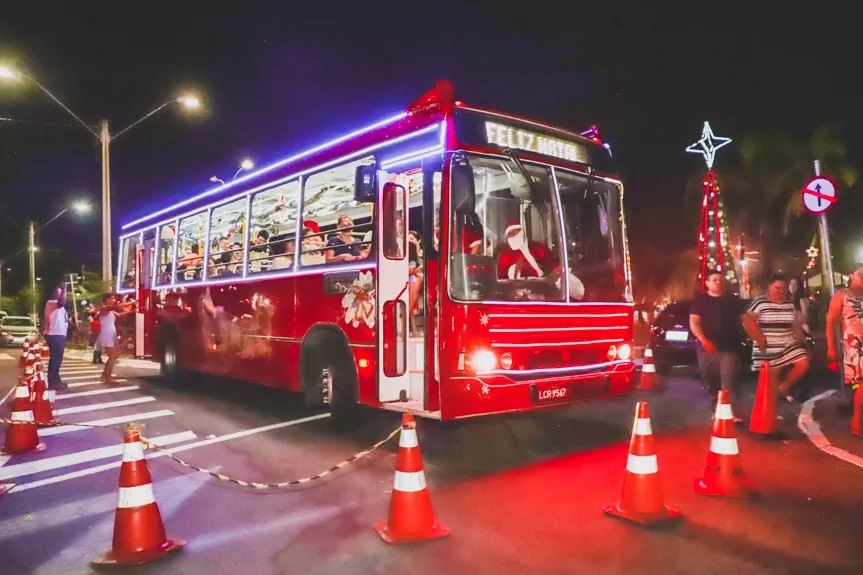 Ônibus vermelho e iluminado e parado, pronto para partir para um passeio natalino pelas ruas da cidade.