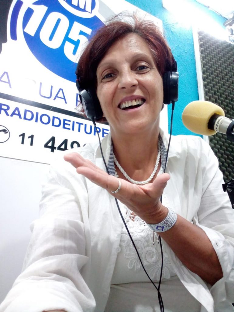 Selfie da Glaucia Gonçalves, em frente ao microfone, com espuma amarela, e ao fundo o logo da rádio '105,9fm' de Itupeva.