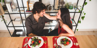 Dia dos Namorados em Bauru: opções especiais de delivery e retirada para curtir em casa. Homem e mulher sentados em uma mesa posta com pratos, como em um jantar em casa.