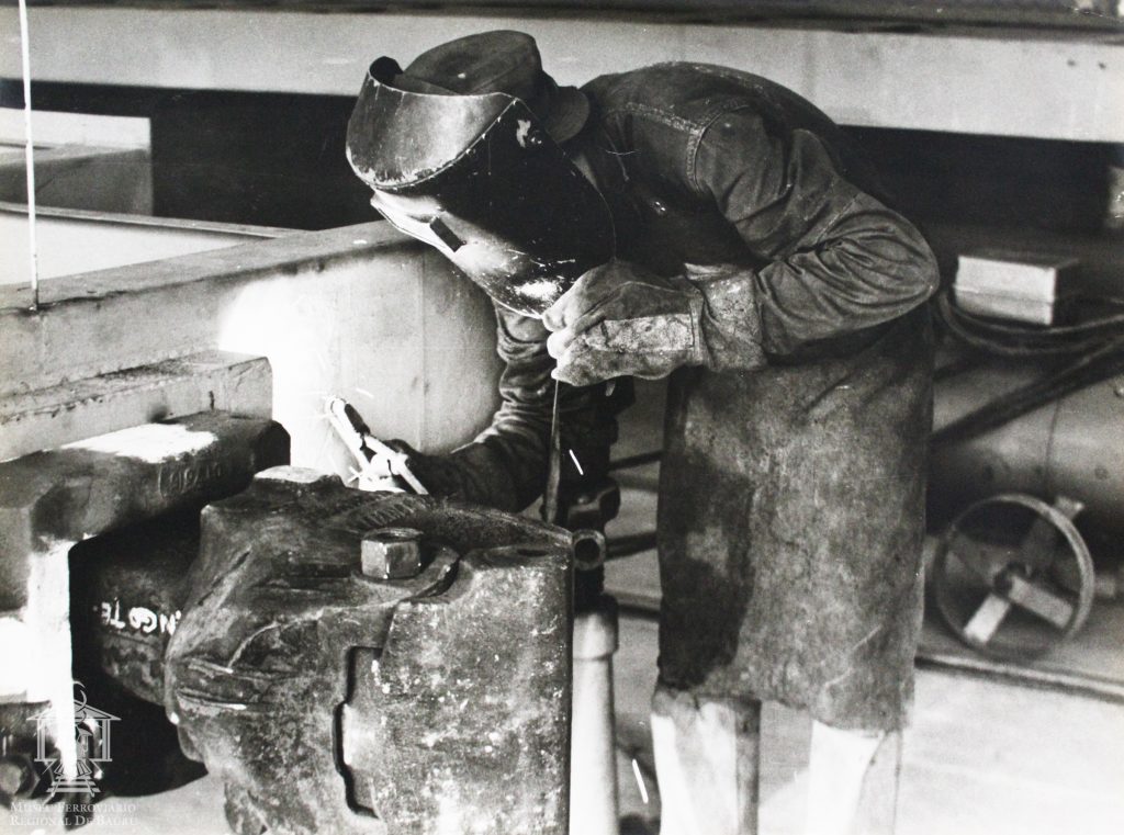 Fotografia com imagem de soldador durante execução de serviço em estrutura de carro de passageiros. Fotos históricas exibem trabalhadores das ferrovias em Bauru. Confira!