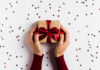 Foto de uma caixa com um laço vermelho de presente em um fundo branco repleto de estrelinhas pequenas. Ideias de presentes de Natal ou amigo secreto no comércio de Bauru