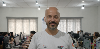 O que é a Solutudo e como funciona a plataforma? Integrante da Solutudo em primeiro plano com equipe trabalhando ao fundo no escritório.