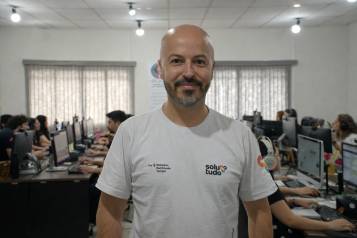 Integrante da Solutudo em primeiro plano com equipe trabalhando ao fundo no escritório.